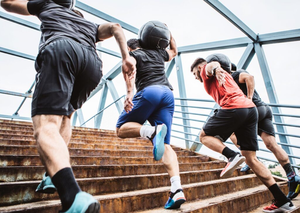 men-taking-part-in-a-corporate-fitness-challenge-carrying-weighted-balls-up-stairs