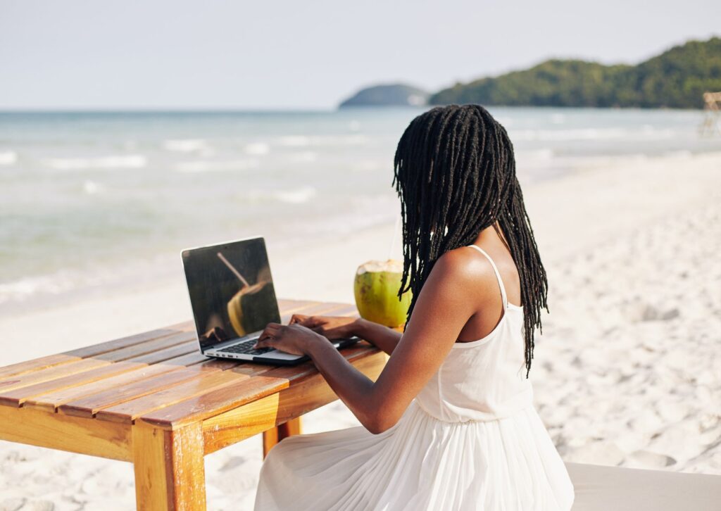 Lady remote working on a beach with a coconut water