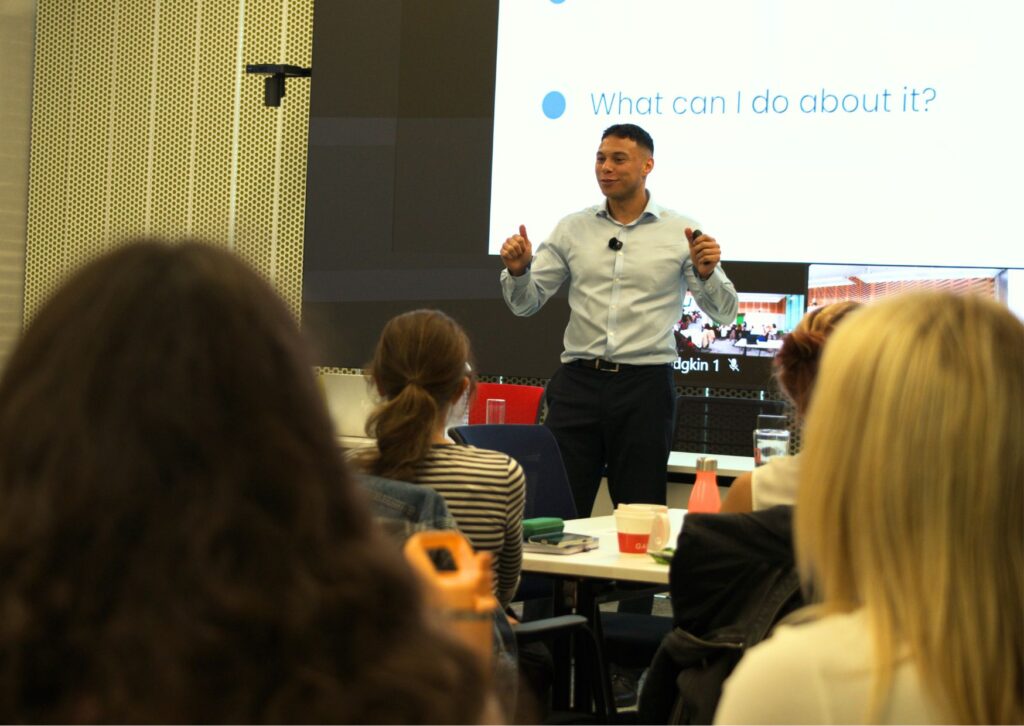 tyler-standing-at-the-front-of-a-meeting-room-smiling-and-delivering-a-team-workshop
